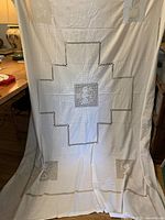 Full view of white embroidered tablecloth showing overall size, drawnwork cross pattern and lace inserts