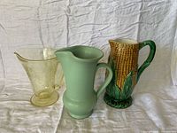 Three pitchers standing side by side on white cloth backdrop