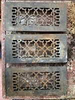 Front view of all three matching cast-iron grate covers showing ornate cut-out pattern and rusted finish