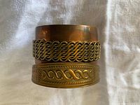 Stacked view of both copper bracelets showing motif patterns and patina