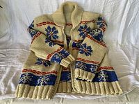 Front view of off-white Cowichan sweater with blue snowflake pattern, red stripes, shawl collar, visible zipper