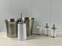 Full set showing both metal waste baskets, toilet brush with stand, two soap dispensers, tumbler