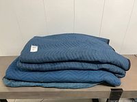 Stack of four blue quilted moving blankets on table