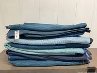 Stack of eight folded blue quilted moving blankets on table