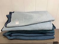 Stack of eight blue moving blankets on surface
