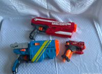 Group shot of two red Mega Magnus, one blue Vortex Vigilon, darts and disc