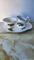 Teacup and creamer on matching tray, showing pattern and gold trim