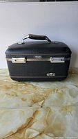Front view of black American Tourister train case with handle and latches visible