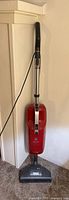 Full view of red Miele Quickstep stick vacuum leaning against wall showing body, wand, cord and floorhead
