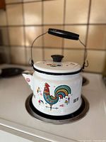 Side view of white enamel kettle showing rooster graphic and handle