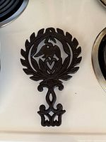 Full view of cast iron trivet on stovetop showing eagle and heart design