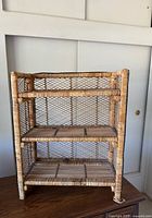 Full front view of rattan bookcase showing three shelves and mesh sides/back