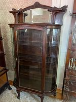 Full view of cabinet showing glass door, curved glass sides, shelves, claw feet