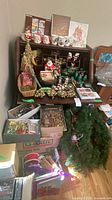 overview of assorted Christmas decor, ornaments, mugs, figurines, wreath, lights, ribbons and boxes