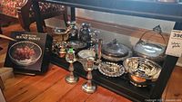 Overview of all silver-plated items on shelf including boxed basket, candlesticks, candelabra, covered dishes, bowls, ladle and vases