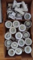 Two boxes containing multiple white recessed pot light fixtures with holders