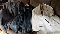 Three jackets laid out: gray suit jacket, black faux leather jacket, beige sport coat