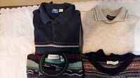 Four folded sweaters: navy collared, cream collared, multicolor patterned, dark fair-isle patterned