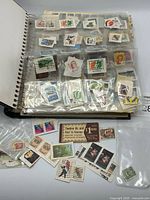 Album open with clear sleeves holding numerous loose stamps and additional loose stamps on surface