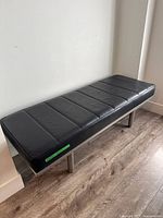 Full view of black leather bench against wall showing legs and upholstery