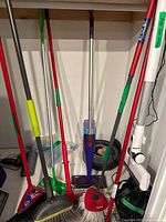 Group of assorted broom and mop handles plus Roomba and vacuum floorhead