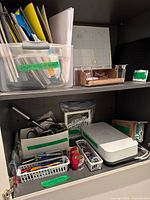 Two-shelf cabinet with plastic bin of folders, letter tray, calendar board, printer and assorted office supplies