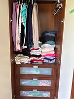 Wardrobe interior showing hanging tops and folded stacks of sweaters, tanks and leggings
