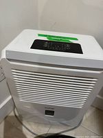 Front view of white portable dehumidifier showing grille, bucket area, attached cord