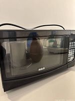 Front view of RCA microwave showing door, viewing window, control panel, attached power cord