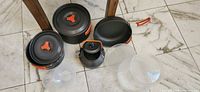 Cookware pieces laid out: two pots, kettle, four clear plastic bowls/plates, detachable handle