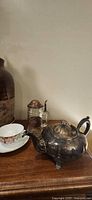 Silver-plated teapot, glass stein, and floral teacup on surface