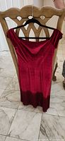 Front view of red velvet off-shoulder dress with fringed hem on hanger