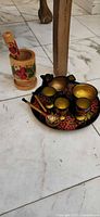 Mortar with pestle beside tray set showing cups, spoons, pitcher, bowl