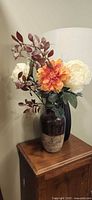 Ceramic vase with artificial flower arrangement displayed on wooden table