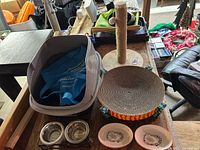 All cat supplies laid out: litter box, scratching bowl, scratching post, stainless bowls, pink bowls