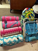 Group shot showing four rolled beach mats, colourful boogie boards, folded blue beach chair