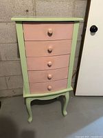 Front view of chest showing five pink drawers and green frame