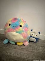 Large tie-dye octopus and small blue/white horned Squishmallows on floor
