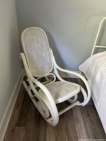Full view of white wood and cane rocking chair beside bed