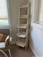 Full view of white wooden ladder shelf in corner showing five tiers and painted finish