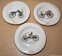 Front view of three ashtrays showing automobile illustrations and gold rims