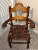 Full view of wooden armchair with painted crest, woven leather seat and metal-braced arms