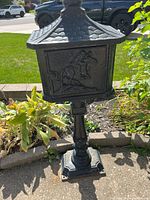 Full view of cast iron pedestal mailbox from front showing relief design and overall condition