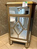 Front view of mirrored side table showing drawer, door, gold trim, acrylic knob