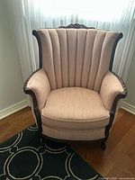 Front view of blush pink wingback armchair showing channel-tufted back and carved wood frame