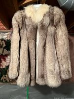 Front view of hip-length blonde fur jacket on hanger