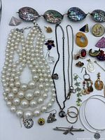 Overview of lot showing pearl necklaces, abalone necklace, chain necklace, many earrings and brooches