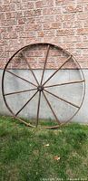 Full view of wagon wheel leaning against brick wall showing 12 spokes and iron rim