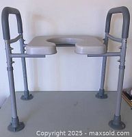 Front view of raised toilet seat showing seat opening, armrests, adjustable legs, suction feet