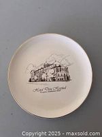 Front of white ceramic plate showing brown illustration, caption and gold rim